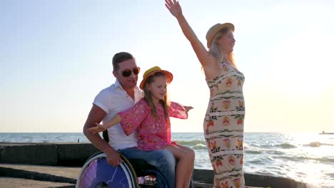 Familie-spielen-Flugzeug-Hände-erhoben-zusammen-auf-Hintergrund-blauer-Himmel,-kleine-Mädchen-auf-Papa-im-Rollstuhl-sitzend