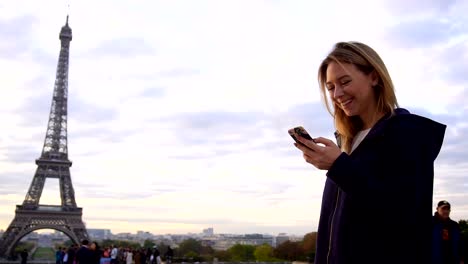 Fröhliche-Frau,-die-im-Chat-per-Smartphone-mit-Eiffelturm-Hintergrund