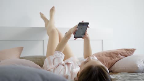 una-joven-charlar-con-los-amigos-en-las-redes-sociales-con-un-teléfono-móvil-en-sus-manos,-ella-está-tumbada-en-la-cama-por-la-mañana