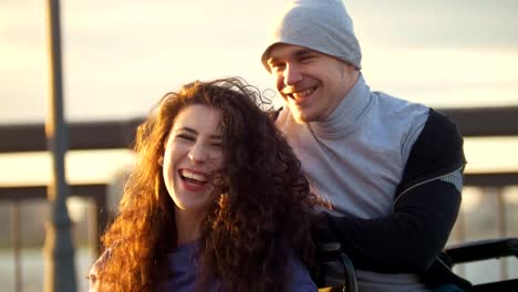 Happy-couple---young-woman-with-disabled-man-in-wheelchair-rests-together-outdoors