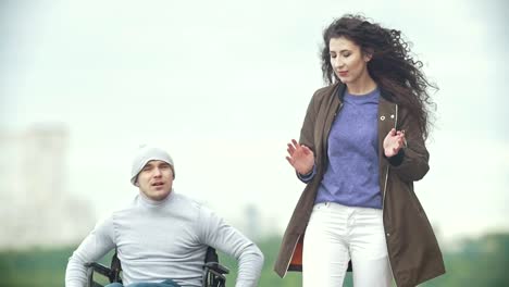 Hombre-discapacitado-en-silla-de-ruedas-con-mujer-joven-caminando-en-la-calle-habla