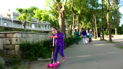 Little-child-learning-to-ride-a-scooter-in-a-city-park