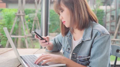 Business-freelance-Asian-woman-working,-doing-projects-on-laptop-and-using-smartphone-while-sitting-on-table-in-cafe.-Lifestyle-smart-beautiful-women-working-at-coffee-shop-concepts.