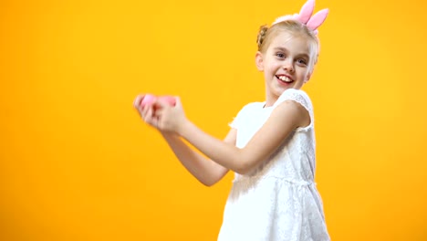 Excited-little-girl-playing-with-colored-Easter-eggs-yellow-background-childhood