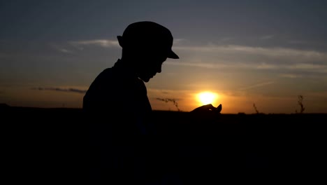 Silhouette-eines-jungen-verwendet-eine-Tablette-bei-Sonnenuntergang-im-Feld-liest-etwas-auf-dem-Tablet-im-freien