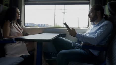 Corporate-employees-man-and-woman-or-coworkers-enjoying-conversation-while-they-using-their-gadget-on-train-compartment-commuting-to-office