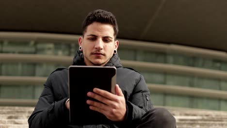 Thoughtful-young-man-using-tablet-while-sitting-outdoor.