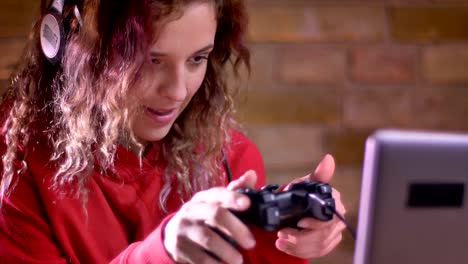 Close-up-portrait-of-young-female-blogger-actively-playing-video-game-using-joystick-on-bricken-wall-background.