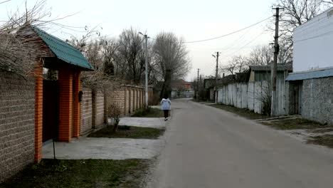 Sola-mujer-camina-a-lo-largo-de-la-carretera-entre-las-casas-y-los-árboles.