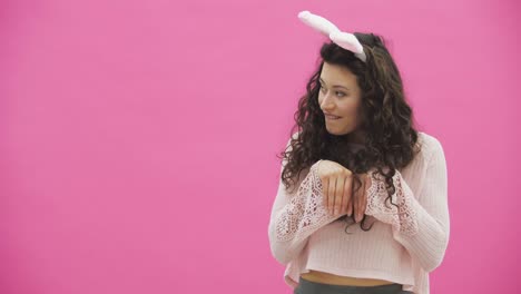 Beautiful-young-girl-standing-on-a-pink-background.-During-this,-there-are-ears-of-rabbits-on-the-head.