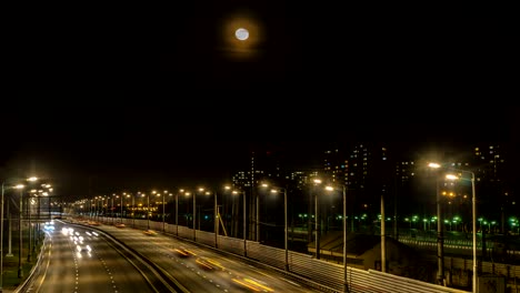 Der-Mond-steigt-über-die-beleuchtete-Autobahn-und-die-Nachtstadt,-Zeitraffer