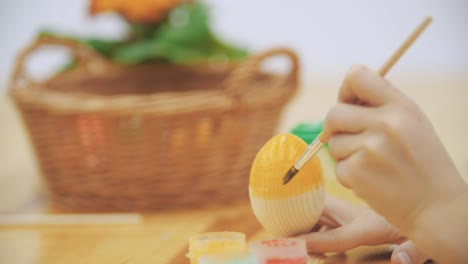 Cheerful-boy-is-painting-an-Easter-egg-in-an-yellow-colour-with-a-help-of-paint-brush.