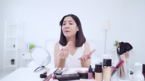 Beauty-Blogger-präsentieren-Beauty-Kosmetik-sitzen-vor-der-Kamera-für-die-Aufnahme-von-Video.-Glücklich-schöne-junge-asiatische-Frau-verwenden-Kosmetik-Rezension-Make-up-Tutorial-übertragen-Live-Video-an-soziale-Netzwerk.