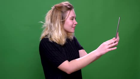 Closeup-portrait-of-young-pretty-blonde-caucasian-female-having-a-video-call-on-the-tablet-with-background-isolated-on-green