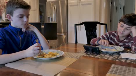 Two-young-boys-eating-breakfast-while-one-watches-videos-on-a-smart-phone