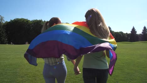 Girlfriends-walking-across-lawn-holding-lgbt-flag