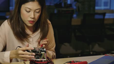 Young-asian-female-electronics-development-engineers-works-with-robot,-measuring-the-signal-in-the-electrical-circuits-of-robotics-prototype-in-workshop.-People-with-technology-or-innovation-concept.