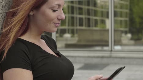 Smiling-Woman-using-smartphone-Sitting-in-business-district,-texting-with-mobile-telephone-outside,-typing-text-message-on-cell-phone.-Paris,-Red-hair.-Social-media.-4K-UHD-Slow-Motion-tilt-up.