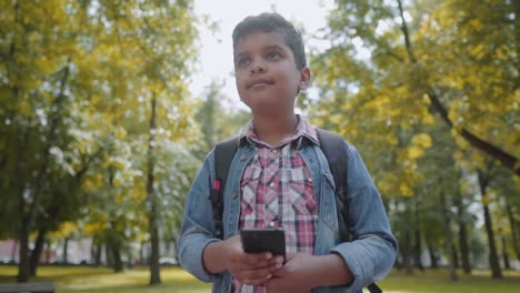 Outdoor-portrait-afro-american-happy-school-boy-with-smartphone.-Young-student-looking-at-mobile-phone.-Back-to-school-concept.-Slow-Motion-Shot