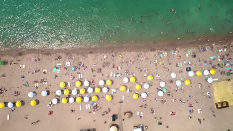 Aéreo:-vista-superior-de-la-playa.-La-gente-se-baña-en-el-mar,-en-la-orilla-sombrillas-de-playa-de-madera