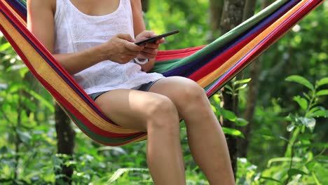 Woman-relaxing-in-hammock--reading-ebook-in-tropical-rainforest