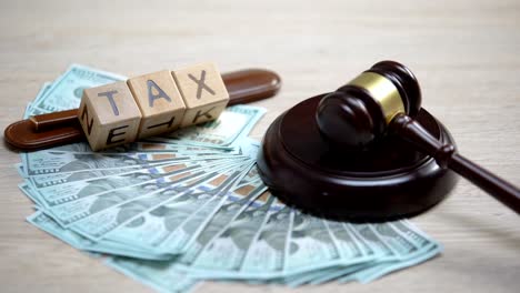 Dollars-and-tax-word-made-of-wooden-cubes-table,-gavel-striking-on-sound-block