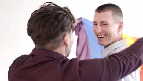 Gay-couple-holding-pride-flag.-In-bedroom.-Dancing-happily.