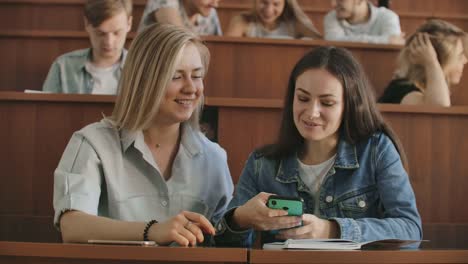 Alumnas-con-un-teléfono-inteligente-en-las-manos-riendo-en-la-audiencia-durante-un-descanso-para-una-conferencia-en-la-Universidad