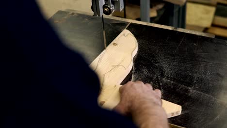 Close-up-footage-of-male's-hands-working-with-an-electric-cutting-machine.-High-angle-footage-of-a-man-cutting-a-fish-shape-wooden-pattern-on-a-table.-Footage-from-the-shoulder