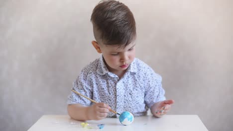 Un-niño-pinta-un-huevo-de-pascua-en-la-mesa-sobre-un-fondo-blanco.