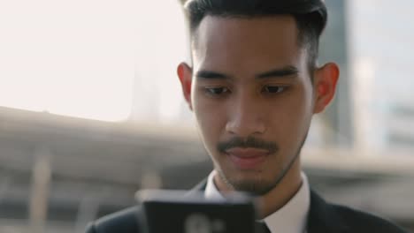 Portrait-handsome-young-businessman-using-a-smartphone-texting-checking-email-messages-online-and-uses-social-networks-while-standing-on-the-street-urban.