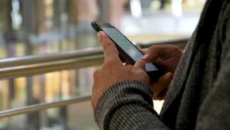 Primer-plano-de-las-manos-del-hombre-enviando-un-mensaje-sobre-el-fondo-del-centro-comercial.-Medio.-Manos-masculinas-usando-su-teléfono-inteligente-para-chatear-en-la-red-social