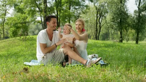 CLOSE-UP:-Adorable-Eltern-mit-schönen-Mädchen-sitzen-auf-Decke-im-park