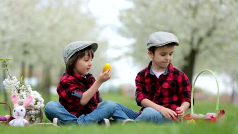 Two-children,-boy-brothers,-having-fun-with-easter-eggs-in-the-park,-beautiful-spring-blooming-garden