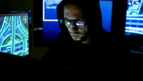 IT-professional-programmer-in-glasses-is-working-on-computer-in-cyber-security-center-filled-with-display-screens-Male-hacker-working-on-computer