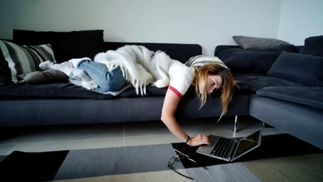 Bored-young-woman-lays-on-couch-chats-on-social-media-laptop