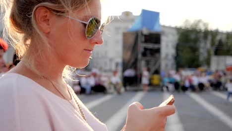 Frauen-Blondine-in-Gläsern-sieht-im-Telefon-unter-freiem-Himmel-in-die-Innenstadt-von-Close-up