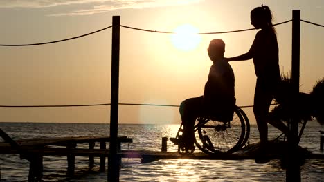 lovely-girl-talk-with-happy-disabled-and-looking-in-skyline-on-background-of-sunset-over-river