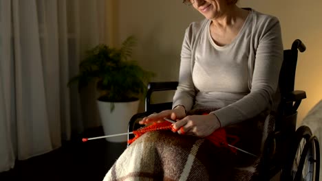 Happy-woman-in-wheelchair-knitting,-thinking-about-grandchildren-and-smiling