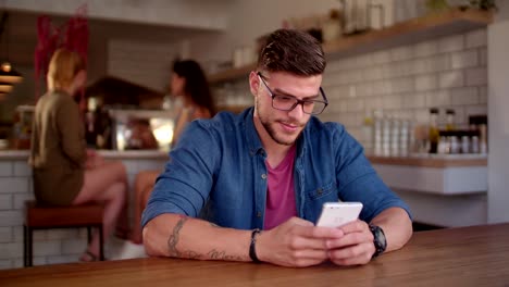 Young-hipster-man-texting-on-mobile-phone-at-urban-cafe