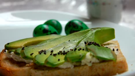 Sandwich-with-avocado-sprinkled-with-black-sesame-on-a-background-of-Easter-eggs