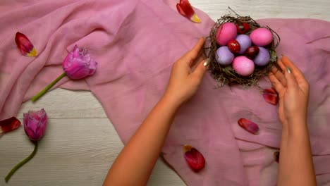 Hände-auf-den-Tisch-gelegt,-ein-Osternest-mit-bunten-Eiern-und-ein-Tablett-mit-Tee