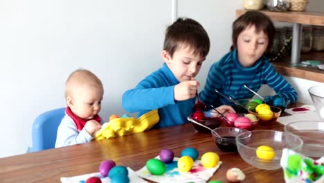 Three-children,-brothers,-coloring-and-painting-easter-eggs-at-home-in-kitchen-for-the-holiday