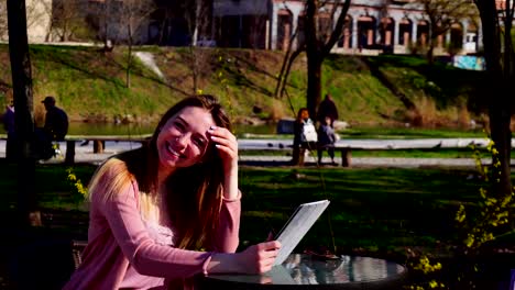 Hübsches-Mädchen-mit-Nahaufnahme-Gesicht-ruhen-im-Frühlingspark-mit-Tablet-und-Blick-in-die-Kamera