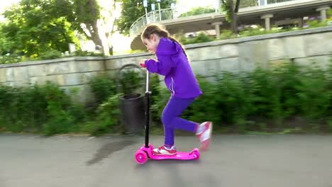 Little-child-learning-to-ride-a-scooter-in-a-city-park