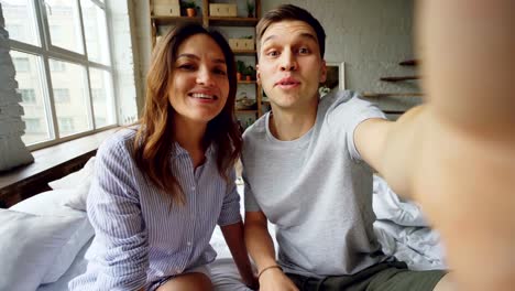 Point-of-view-shot-of-happy-couple-famous-bloggers-recording-video-for-their-followers-at-home.-Young-people-are-talking-and-gesturing-looking-at-camera.