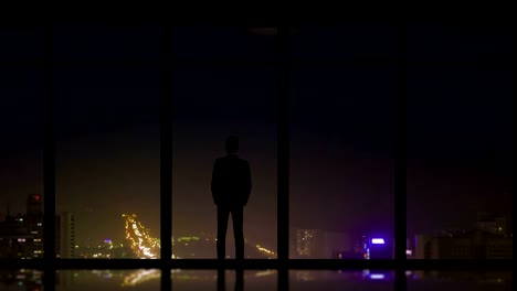 El-hombre-pie-cerca-de-una-ventana-panorámica-en-el-fondo-de-la-ciudad-de-noche