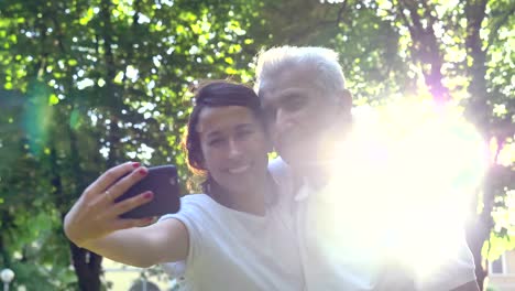 Una-niñera,-enfermera,-cuidar-de-los-ancianos,-una-chica-(mujer)-y-el-abuelo-se-sientan-en-un-libro-de-bolsillo-y-hacer-selfie,-en-el-parque.