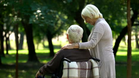 Lady-talking-to-disabled-husband,-walking-in-park,-woman-pointing-at-distance