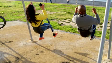 Vista-posterior-de-pareja-jugando-en-columpio-de-parque-infantil-en-el-Parque-4k